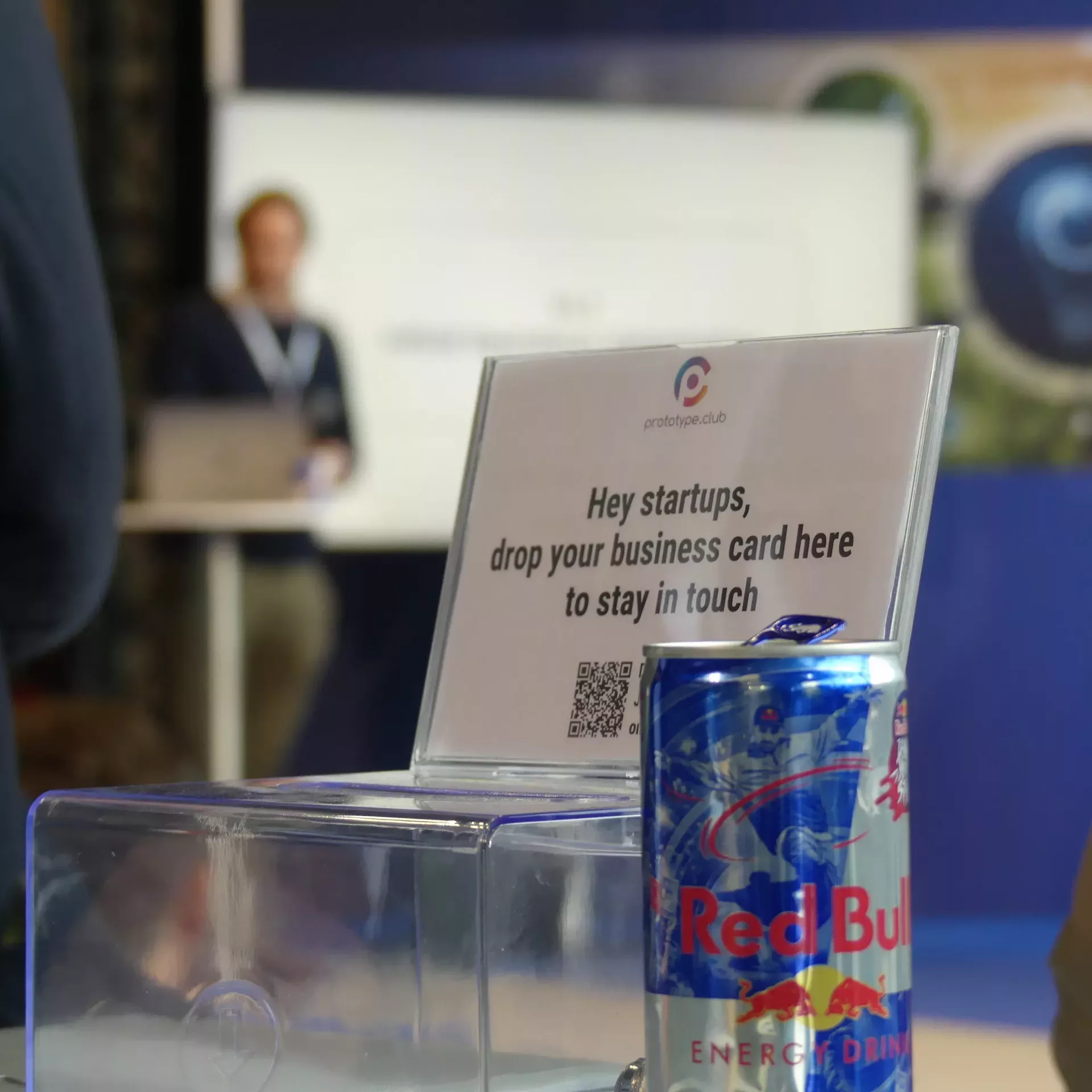 im Vordergrund befinet sich eine RedBull Dose und eine Schachtel in der Startups ihre Visitenkarten hinterlassen können. Der Hintergrund ist verschwommen und zeigt das Messegeschehen.